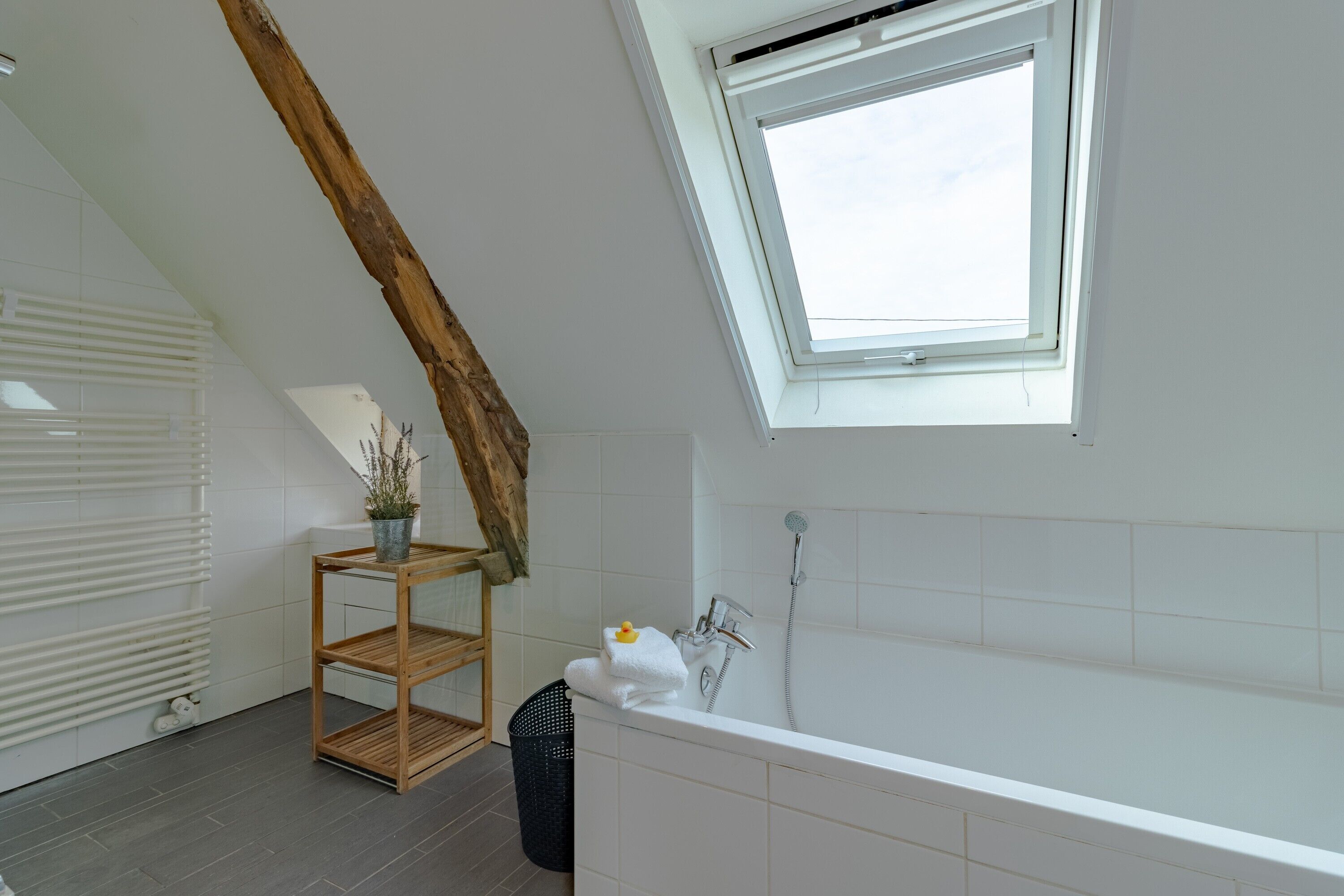 Ein modernes Badezimmer mit Dachfenster, einer Badewanne, einem Holzregal und einer Heizung.