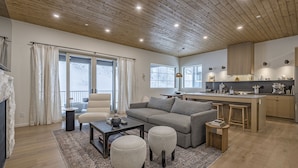 A modern living room with a sofa, ottomans, a coffee table, and a kitchen area with a bar. - Modern Duplex w/ private hot tub, EV charger & media room - pet friendly too! (Silver Star Mountain)
