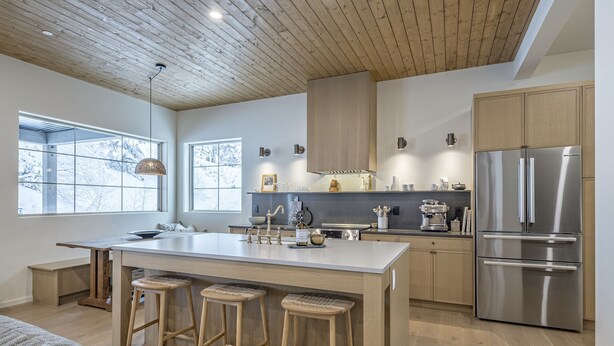 A modern kitchen with a large island, wooden stools, stainless steel appliances, and large windows. - Modern Duplex w/ private hot tub, EV charger & media room - pet friendly too! (Silver Star Mountain)
