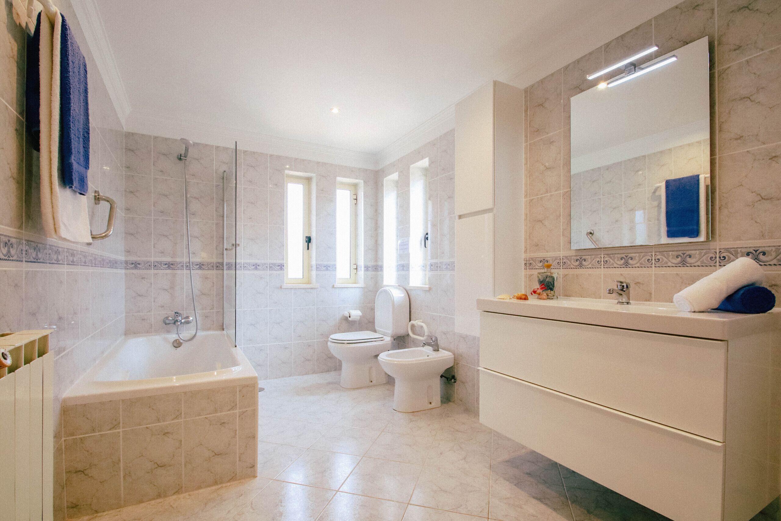 A modern bathroom with a bathtub, two toilets, a vanity with a mirror, and a shower area.