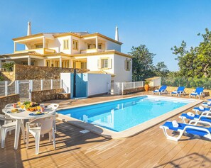 A poolside area with a pool, lounge chairs, a dining table with chairs, and a stone wall.