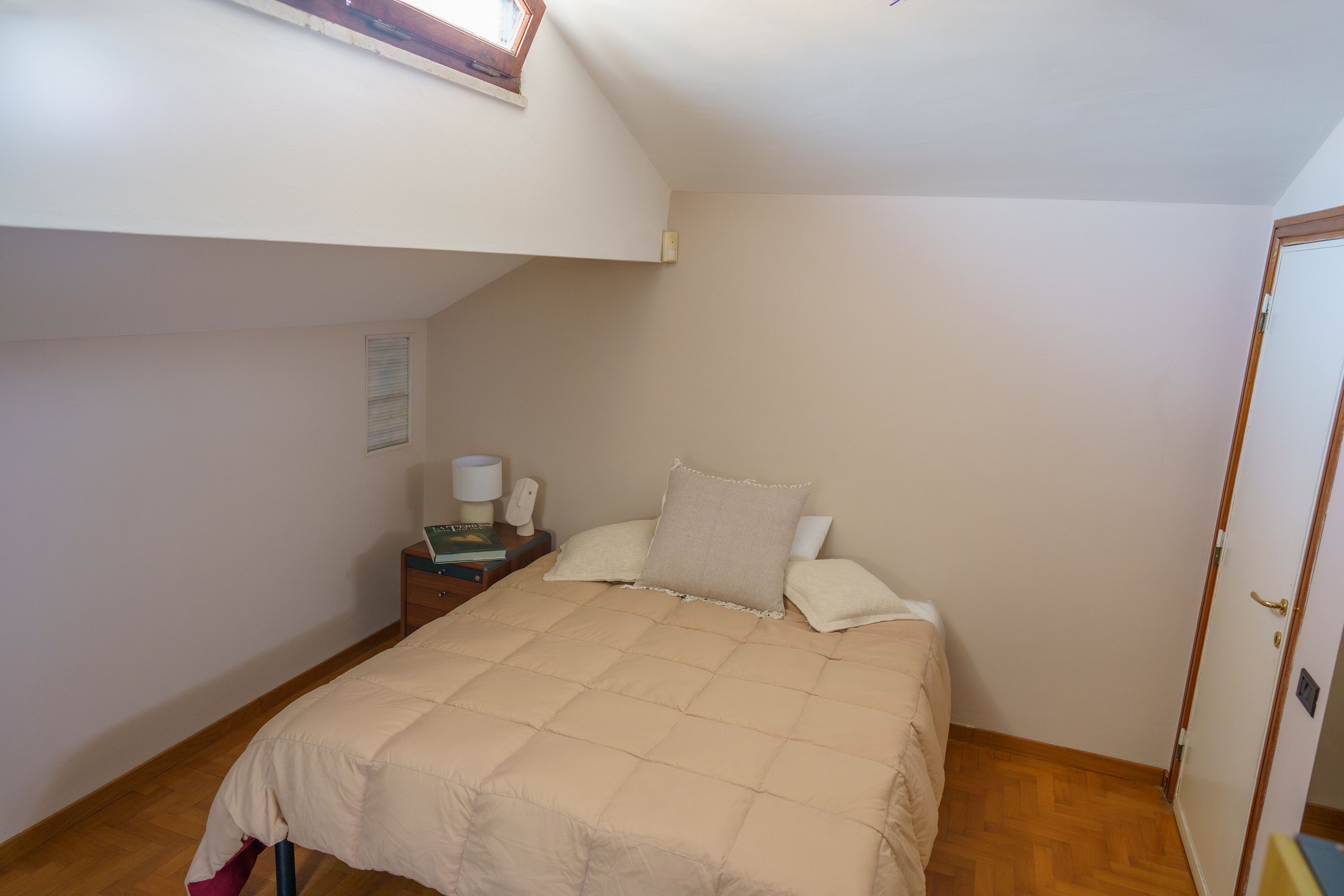 A bedroom with a bed, a nightstand, a lamp, and a window.