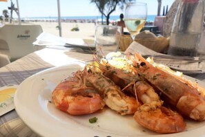 A plate of cooked shrimp on a table with a beach view in the background. - Elegant Spacious Villa in Serene Roman Oasis -- Family-Friendly (Lazio)