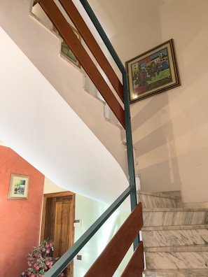 Un escalier avec des marches en bois et une rampe bleue, menant à un palier où se trouvent un tableau encadré et une porte.