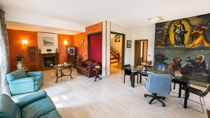 A spacious living room with a fireplace, leather sofas, a dining area with a glass table, and a large painting on the wall.