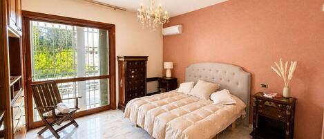 A bedroom with a large bed, a chandelier, a nightstand, a dresser, and a chair.