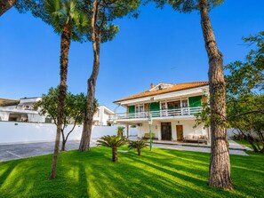 A two-story house with a balcony, surrounded by trees and a well-maintained lawn. - Elegant Spacious Villa in Serene Roman Oasis -- Family-Friendly (Lazio)