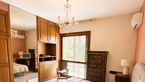 A bedroom with a large bed, wooden wardrobe, a chandelier, and a window.