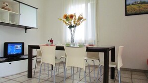 Un coin repas avec une table, des chaises, un vase de fleurs, un ordinateur posé sur un bureau et un tableau accroché au mur.