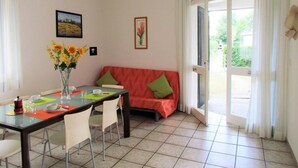 Un coin repas comprenant une table, des chaises, un vase avec des fleurs, un canapé avec des coussins et une vue à travers une porte vitrée.