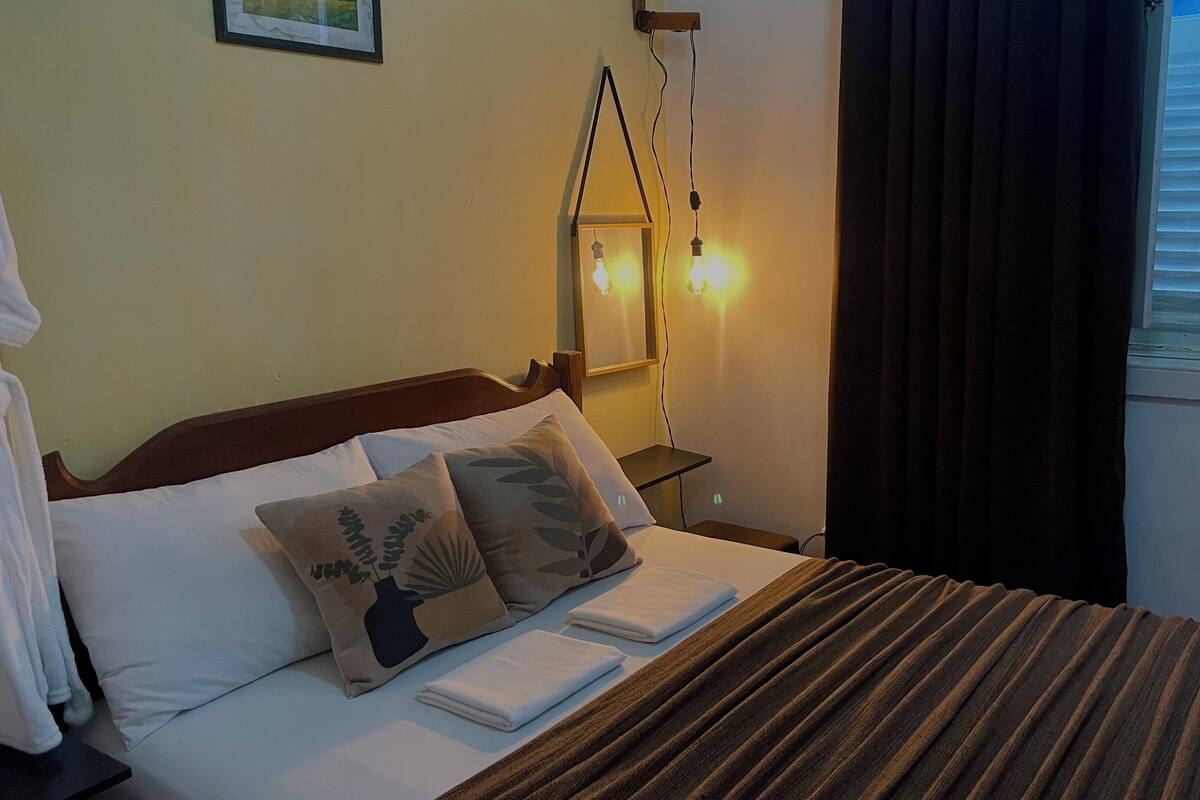 A neatly made bed with pillows, a bedside table, and a wall-mounted light fixture.