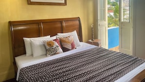 A neatly made bed with a patterned bedspread and several pillows, a wooden headboard, and a framed painting on the wall. - Panorama Inn (Rio de Janeiro)