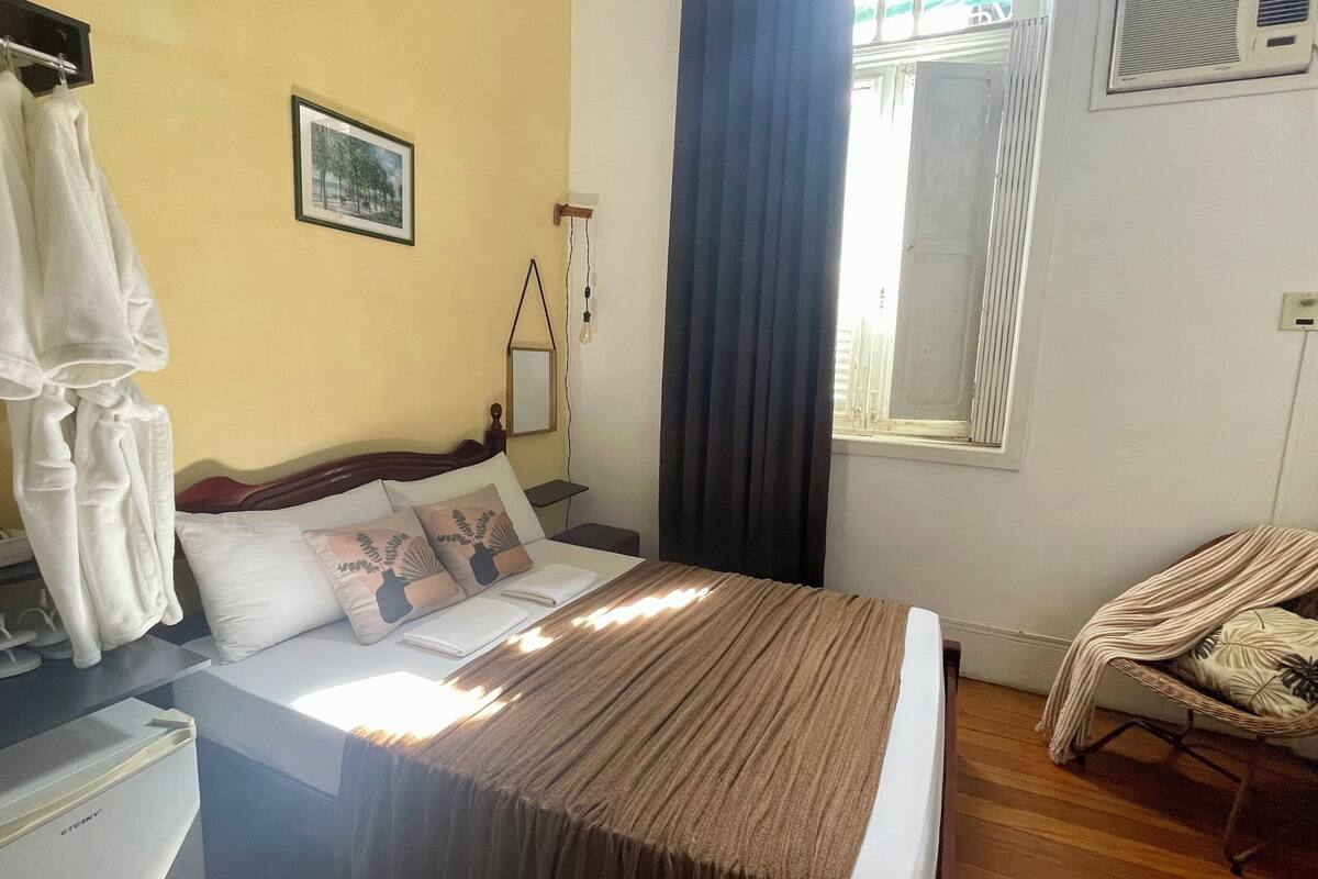 A hotel room with a bed, a chair, a desk, and a window.