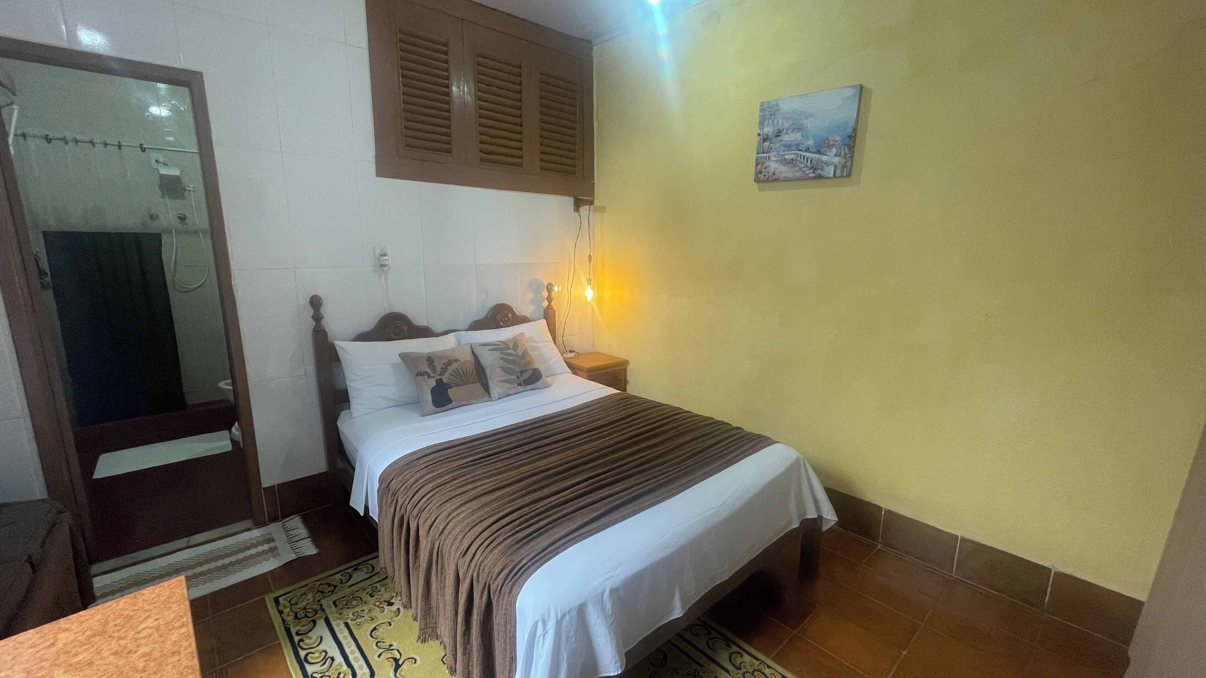 A bedroom with a bed, bedside table, and a wall-mounted light fixture.