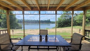 A covered outdoor seating area with a table and chairs, overlooking a lake and forested area. - Pickwick- Screened Patio ON Tennessee River 7th Nt FREE- Dogs Allowed

 (Morris Chapel)