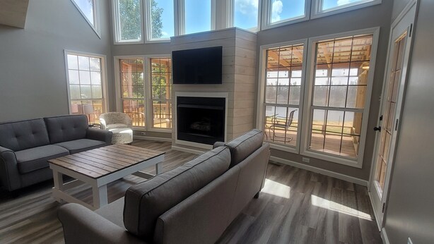 A spacious living room with a fireplace, large windows, and a flat-screen TV. - Pickwick- Screened Patio ON Tennessee River 7th Nt FREE- Dogs Allowed

 (Morris Chapel)