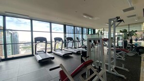 A gym with treadmills, weight machines, and large windows offering a city view.