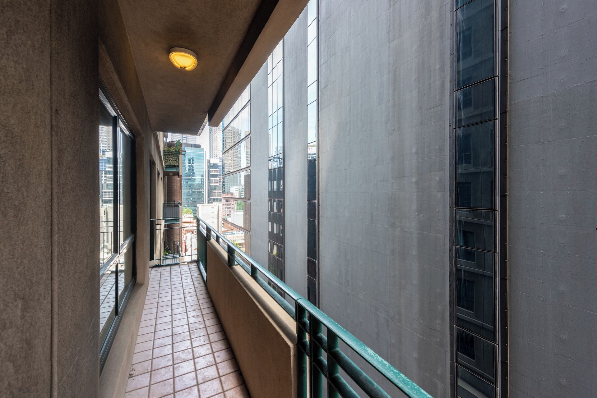 A corridor with tiled flooring, a green railing, and large windows.