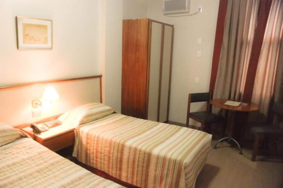 A hotel room with two beds, a desk with a lamp, a chair, and a small table.
