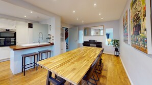 A modern kitchen with a wooden dining table, built-in oven, and a piano. - Bannister House | Oxford Holiday Let | 5 Beds & Sleeps 9 (Oxford)