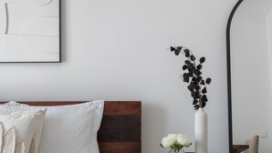 Une chambre à coucher avec un lit, une table de chevet ornée d’un vase de fleurs, un miroir et un tableau encadré accroché au mur.