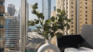 Un balcon donnant sur une vue de la ville, une plante en pot, une bougie et une chaise en osier.