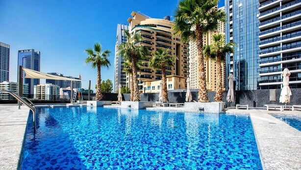 Une piscine à l’eau d’un bleu cristallin, entourée de palmiers et de bâtiments modernes.