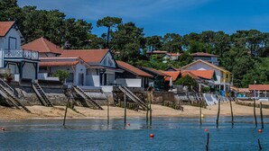 A coastal residential area with houses, a sandy beach, and wooden walkways leading to the water. - Holiday Home 'Villa Cap Ferret Centre Ref 222' with Private Terrace (CAP-FERRET)