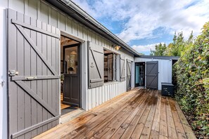 A building with large wooden doors, a wooden deck, and a garden area.