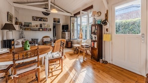 A wooden dining table with chairs, a television, and a bookshelf in a room with white walls and wooden floors. - Holiday Home 'Villa Cap Ferret Centre Ref 222' with Private Terrace (CAP-FERRET)