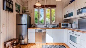 A modern kitchen with white cabinets, stainless steel appliances, a wooden bench, and a view through large windows. - Holiday Home 'Villa Cap Ferret Centre Ref 222' with Private Terrace (CAP-FERRET)