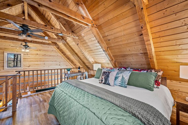 A cozy attic bedroom with a wooden ceiling, a bed with multiple pillows, and a small table with a lamp. - The Willows (Sevierville)