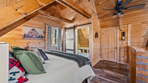 A wooden cabin bedroom with a bed, pillows, a ceiling fan, and a wooden staircase. - The Willows (Sevierville)
