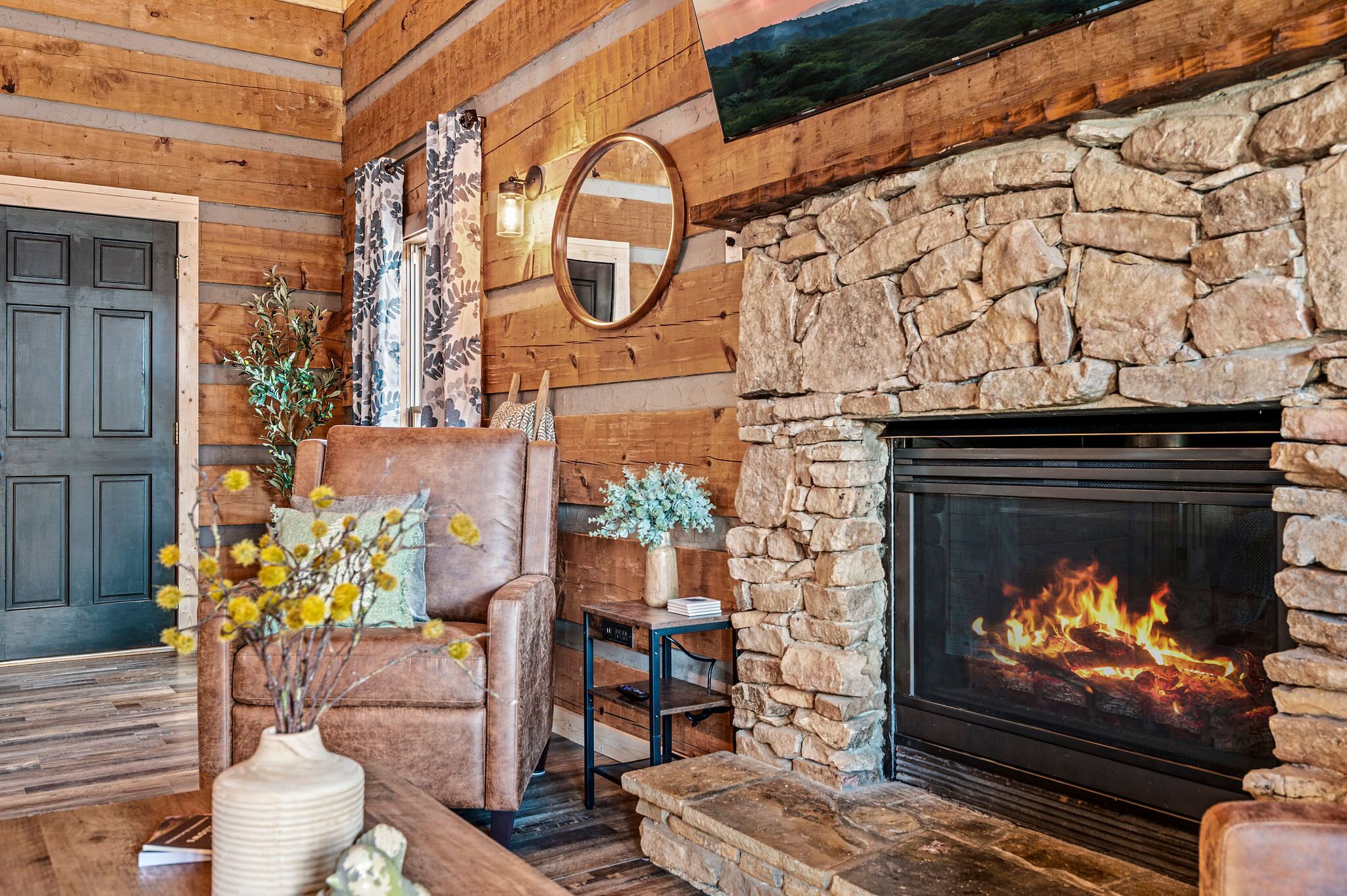 Una sala de estar acogedora con chimenea de piedra, paredes de madera, un sillón de cuero y un florero con flores.