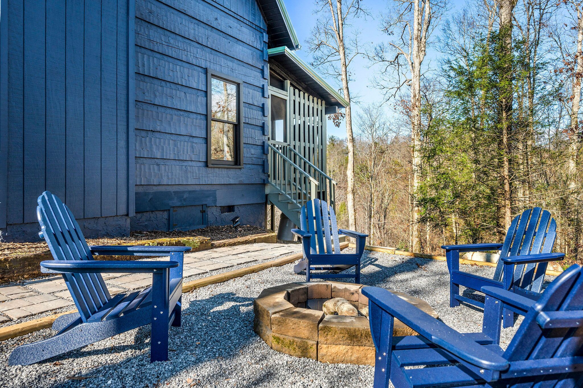 A cabin with a fire pit and Adirondack chairs in front.