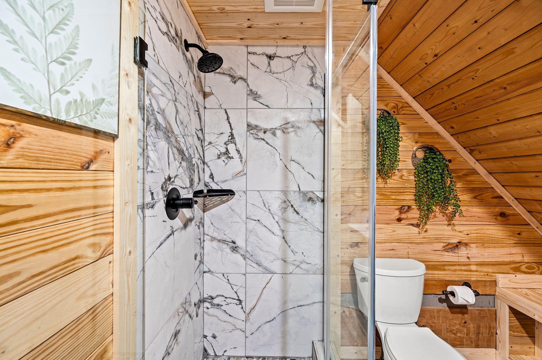 A bathroom with a shower, a toilet, and a sink, all with wooden walls and a marble tile backsplash.