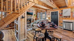 A wooden cabin interior with a staircase, a fireplace, a dining area, and a kitchen. - The Willows (Sevierville)