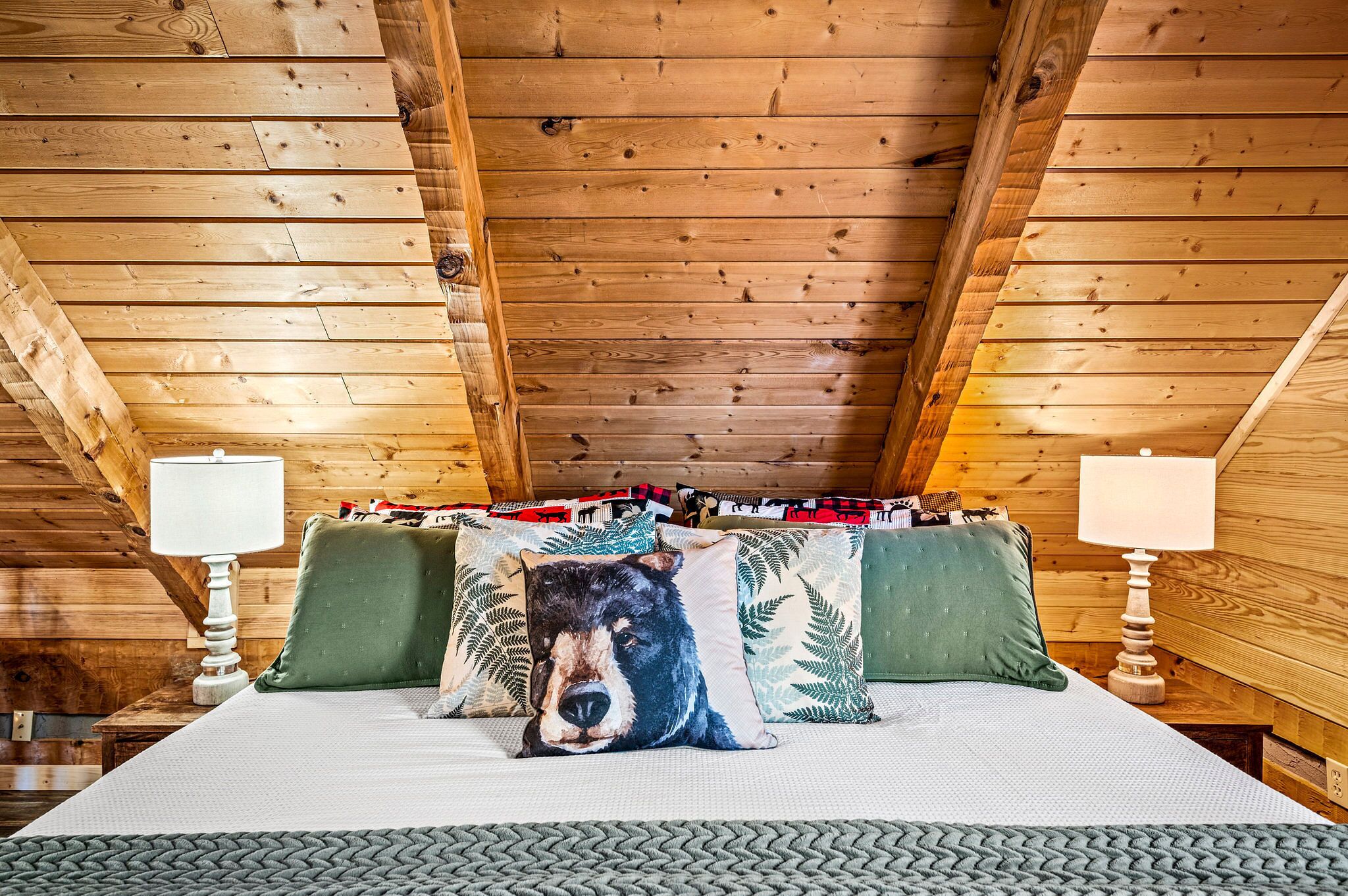 Un plafond en bois à pente douce, un lit avec un matelas et des oreillers blancs, et deux lampes de chevet.