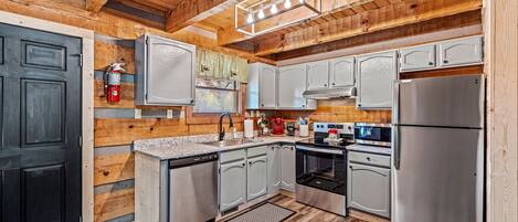 A modern kitchen with wooden walls, stainless steel appliances, and a black door.