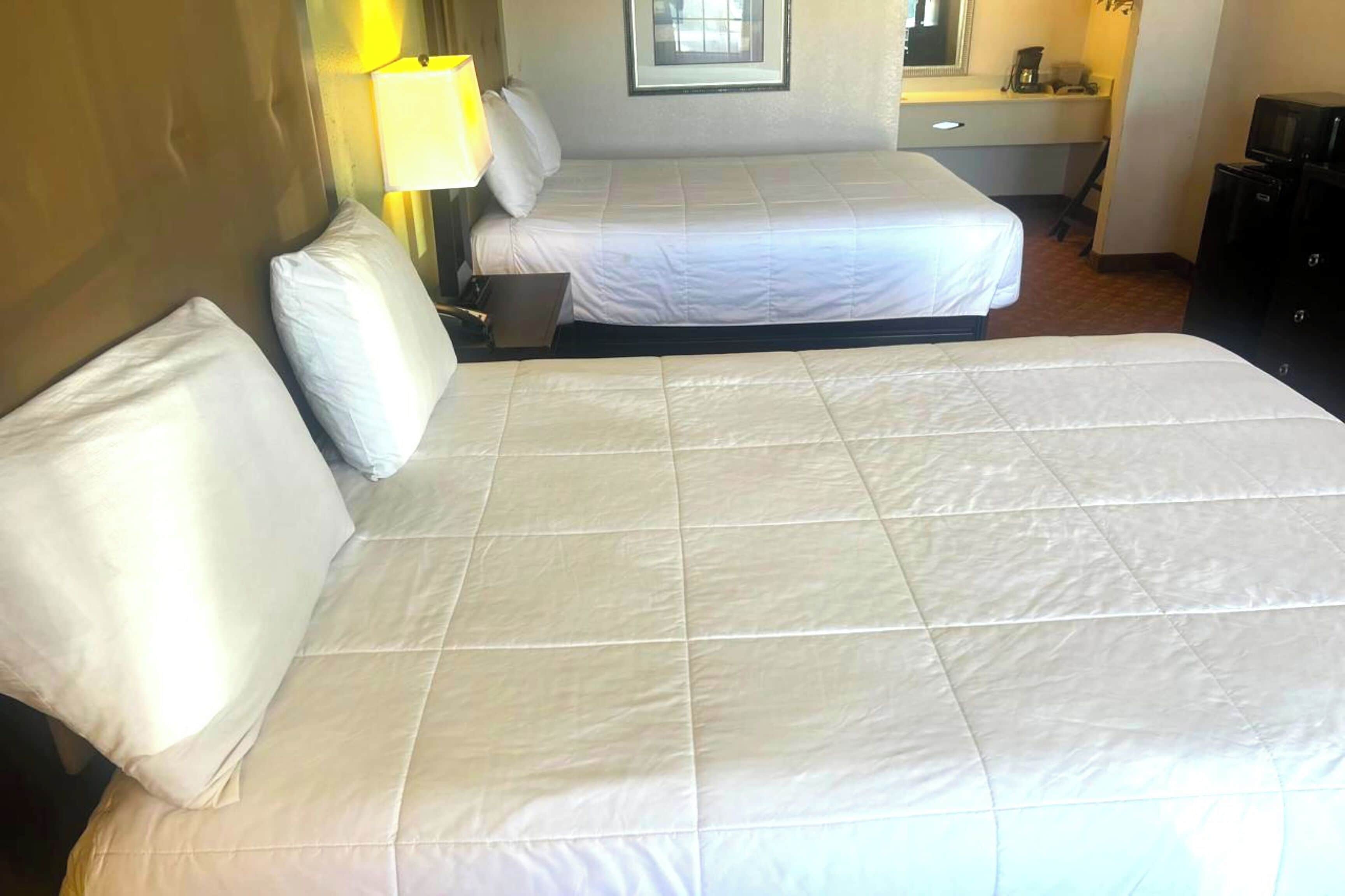 Ein Hotelzimmer mit zwei Betten, einem Schreibtisch, einem Sessel, einer Lampe und einem Fernseher.