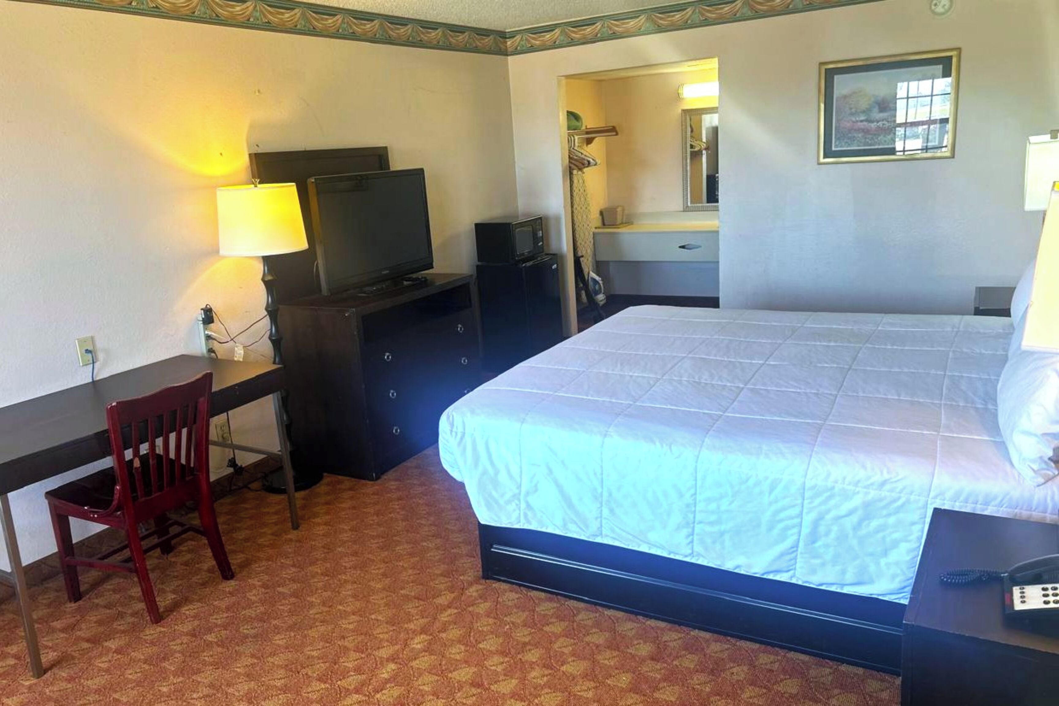 Habitación de hotel con cama, escritorio, silla, televisión y una pequeña mesa con teléfono.
