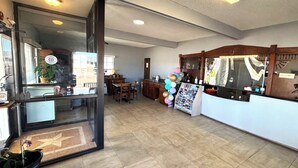 Una habitació espaiosa amb un gran finestral, un taulell de recepció de fusta i un paviment de rajoles.