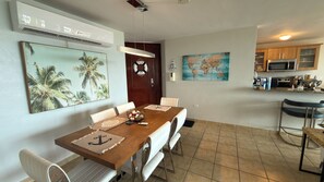 A dining area with a wooden table, white cushioned chairs, a world map on the wall, and a kitchen with wooden cabinets and a microwave. - 608 Ocean & Marina Views 3 Bedroom 2 Bathroom Luxury Condo (Fajardo)