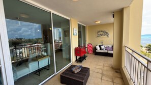 A balcony with a sofa, a red suitcase, and a basket. - 608 Ocean & Marina Views 3 Bedroom 2 Bathroom Luxury Condo (Fajardo)