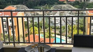 Un balcón con vistas a un puerto deportivo y una noria. Se observa una mesa redonda con una bandeja, vasos y una botella.