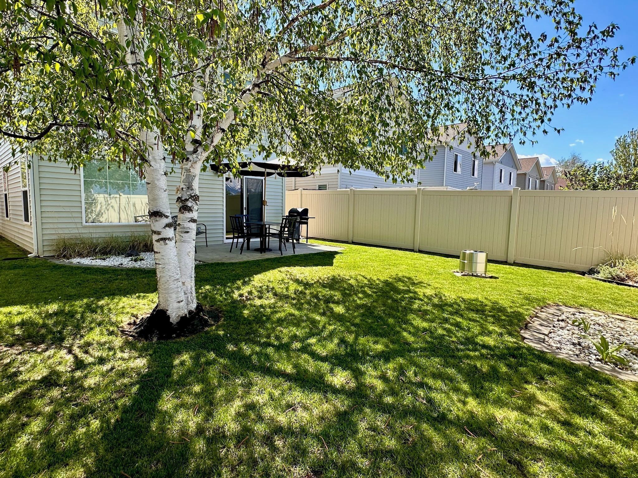 A backyard with a tree, patio furniture, and a white fence.
