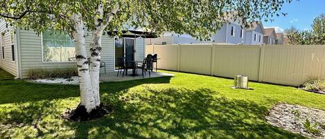 A backyard with a tree, patio furniture, and a white fence.