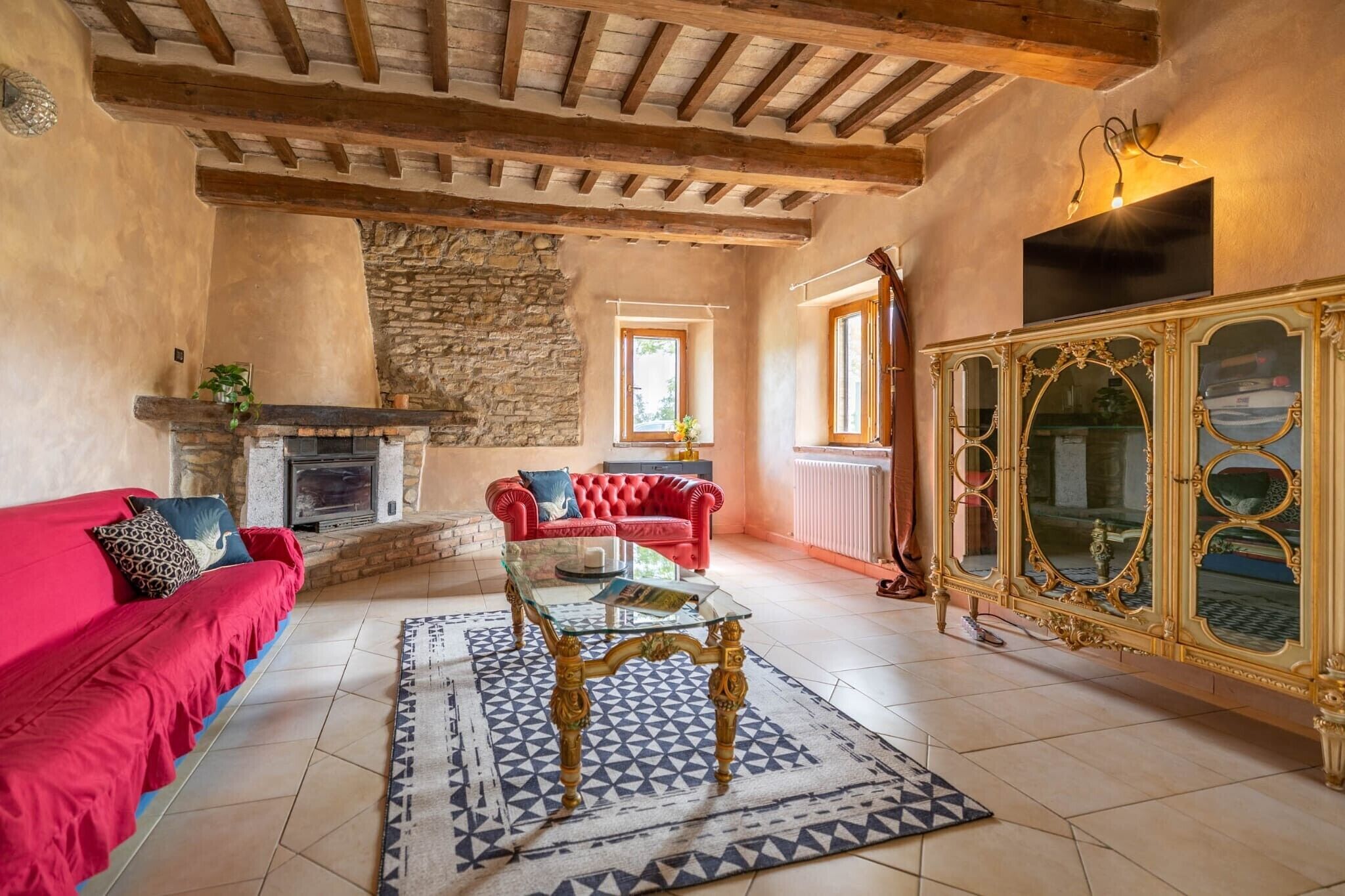 A living room with a fireplace, red sofa, glass coffee table, and ornate cabinet.