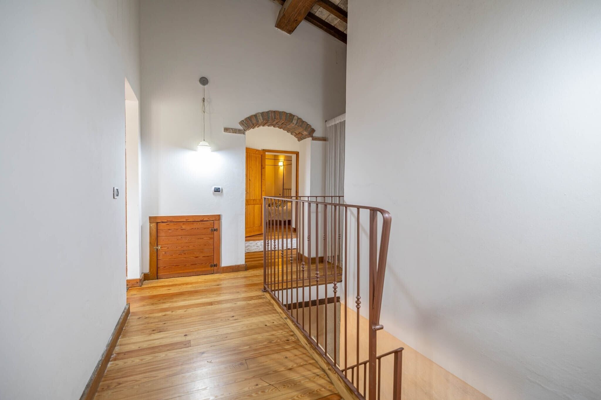 A hallway with wooden flooring, a metal railing, and a wooden door leading to another room.