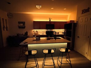 A kitchen with a central island, bar stools, and a microwave.